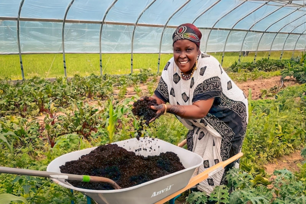 Smiling Somali Bantu woman prepares compost in lush greenhouse garden