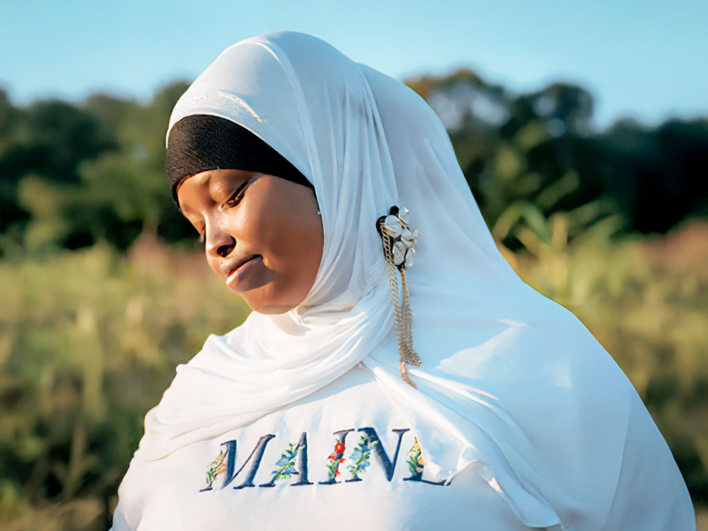 Somali Bantu woman reflects proudly, wearing “MAINE” shirt outdoors