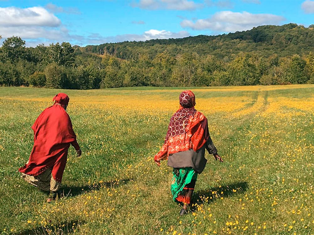 Two Somali Bantu women walking through vibrant, sunlit wildflower field