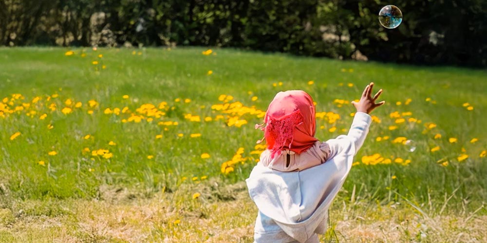 Young Somali Bantu child chasing bubble through sunny flower-filled field